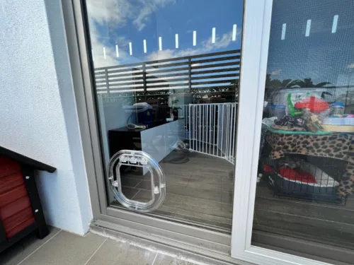 A clear pet door fitted low in the fixed panel of a glass sliding door