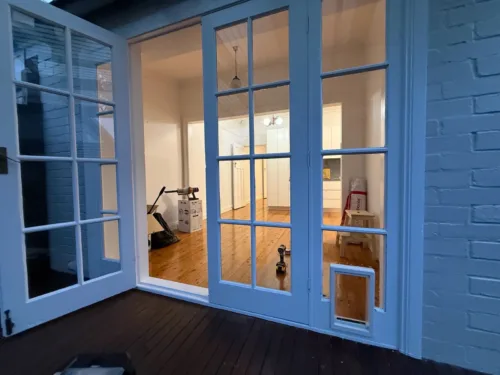 A pet door at the base of blue-grey French doors, seen from inside