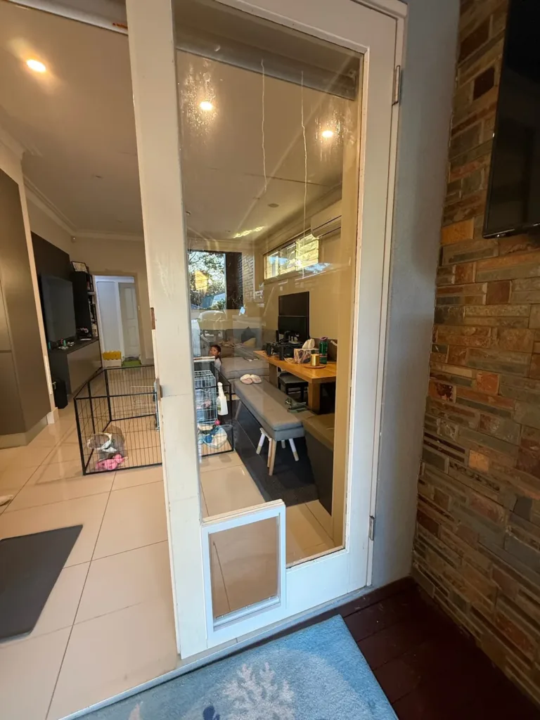 A pet door at the base of a white French door, looking through to a kitchen and dining room