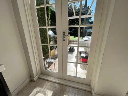 Clear pet door in the lower pane of French doors looking onto a garden