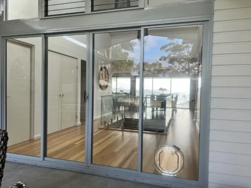 A clear pet door cut into a wide glass sliding door with a water view beyond