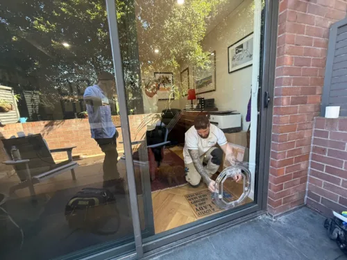 A Sydney Paws installer kneeling at a glass sliding door as the clear pet door is fitted
