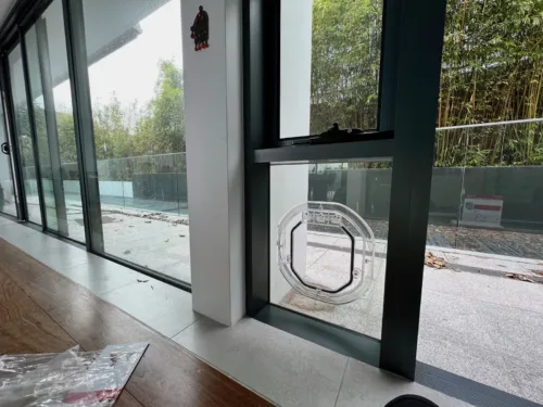 A clear pet door in a glass panel beside a pool fence