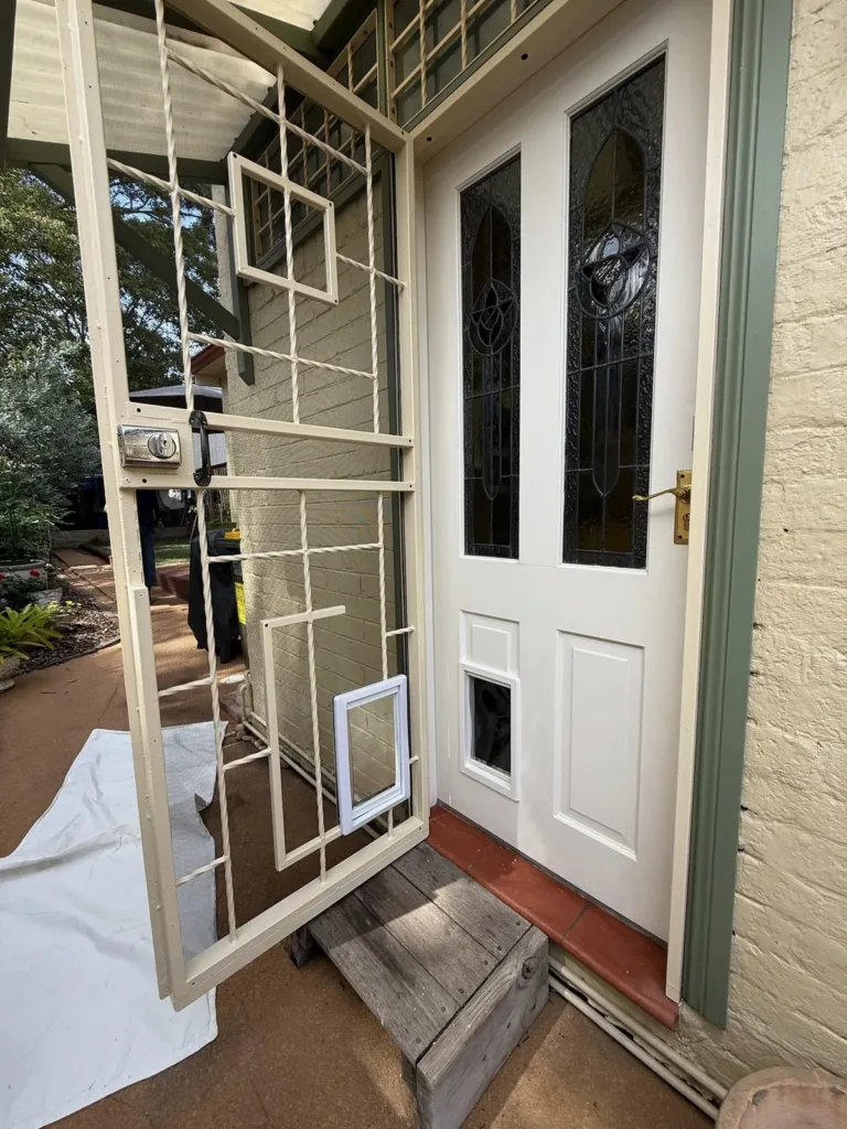 An open cream security door and a white leadlight door, each fitted with a pet door