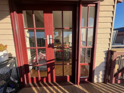 A pet door fitted in red-stained timber French doors opening onto a timber deck