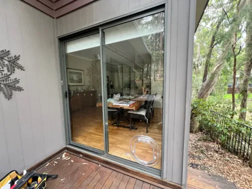 A clear pet door fitted in a silver-framed sliding glass door opening onto a timber deck