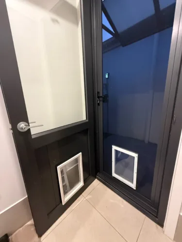 Two white pet doors, one behind the other, in a black security door and the door behind it