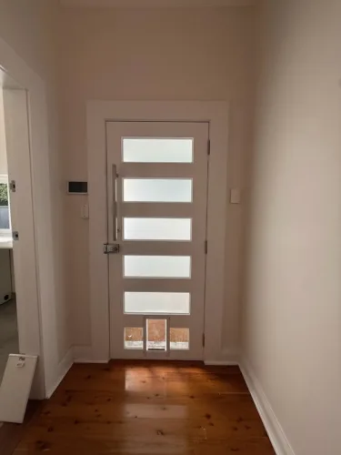A pet door at the base of a white door with horizontal glass panels